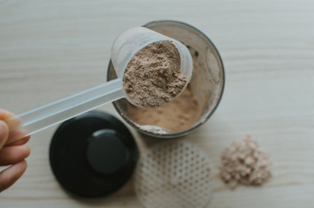woman pours a measuring cup of chocolate protein into a shake to make a shake for athletesの写真素材