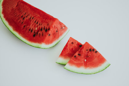 slice of a huge juicy watermelon with black seeds and several chopped pieces on a white backgroundの写真素材