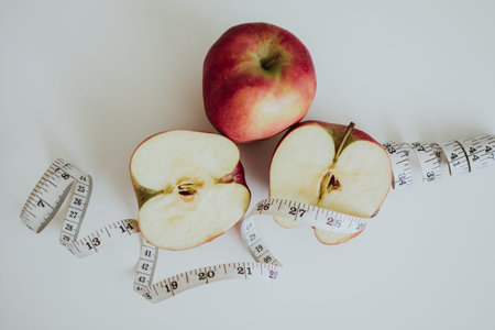 macro shooting of red full and cut in half apples and measuring tape on white background