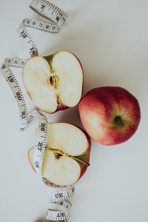 macro shooting of red full and cut in half apples and measuring tape on white backgroundの写真素材