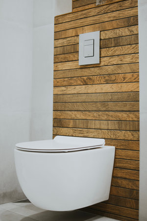 white new toilet and metallic button mounted on the wall against a background of stylish wood tiles
