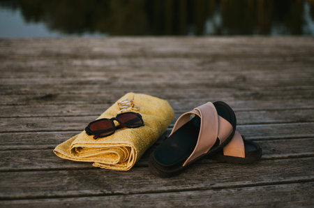towel, sunglasses, hair clip and slippers on a bench near the water for swimming in the summer...