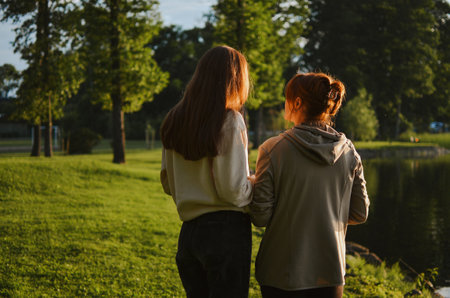 mother and daughter walk together next to the lake and talk in nature in the summer in the eveningの写真素材