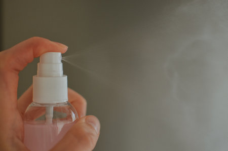 Woman holding cosmetic pink spray bottle, pressing spray mist to spray close-up atomizer.の写真素材