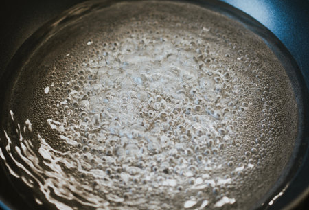 pot with boiling water with bubbles close-up on black kitchen stoveの写真素材