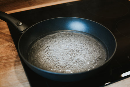 frying pan with boiling water with bubbles close-up on black kitchen stoveの写真素材
