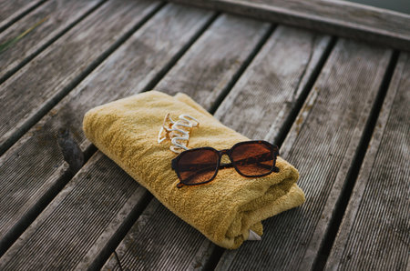 towel, sunglasses, hair clip on a bench near the water for swimming in the summer season on a lakeの写真素材