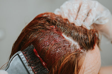 woman applying hair dye with a special brush wearing gloves at home in the bathroomの写真素材