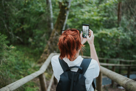 a female traveler goes down the stairs and takes a photo on her phone in the depths of the forestの写真素材