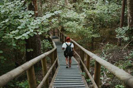 female hiker with a backpack goes down the stairs with railings in the depths of the forestの写真素材