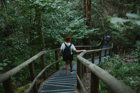 female hiker with a backpack goes down the stairs with railings in the depths of the forestの写真素材