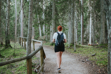 a woman with a backpack goes hiking along a path in the depths of the forestの写真素材