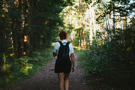 a woman with a backpack goes hiking along a path in the depths of the forest