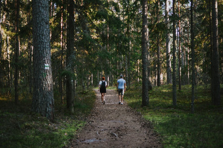 a woman with a backpack and a man are hiking together along a path deep in the forestの写真素材