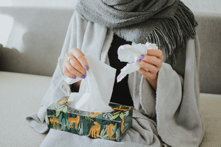 a woman wrapped in a scarf takes out tissues for her nose against the background of medicines
