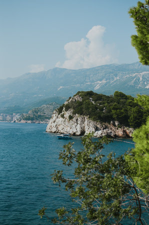 view of rocks with trees and the Adriatic sea with a yacht in Montenegro with the city of Budvaの写真素材