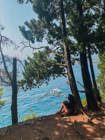 woman enjoying the view from a cliff to the Adriatic sea with a sailing yacht in Montenegroの写真素材