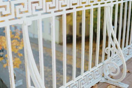 white iron fence with patterns close-up on pedestrian bridge in autumn park with yellowed treesの写真素材