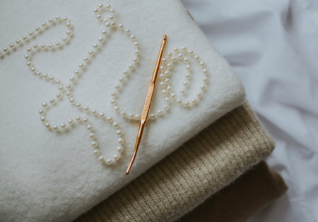 gold crochet hook and beads on white and beige chunky knit fabric close-up for warmth and cozinessの写真素材