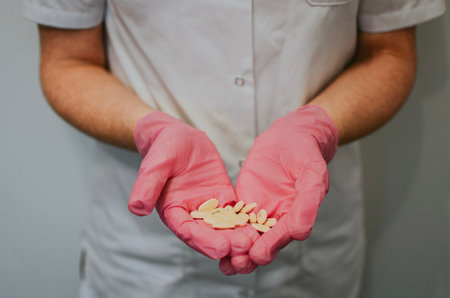 A nurse in a white coat and pink gloves holds yellow tabletsの写真素材