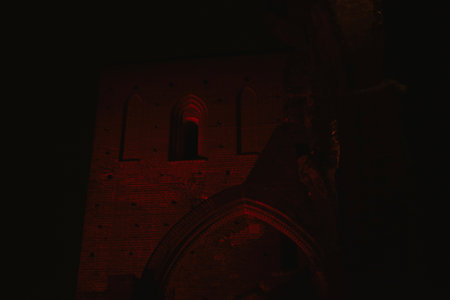 Pointed arch of an old historic brick church with red lighting at night in Europe in a parkの写真素材