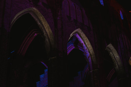 Pointed arch of an old historic brick church with purple lighting at night in Europe in a parkの写真素材