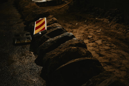 Dug up pedestrian path for repair late at night, stones for the road nearby, warning yellow red signの写真素材