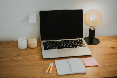 Working wooden table with laptop with black blank screen and calendar, table lamp, candlesの写真素材