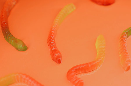 Gummy worms close-up of different sweet flavors for children on a bright orange background. High quality photoの写真素材