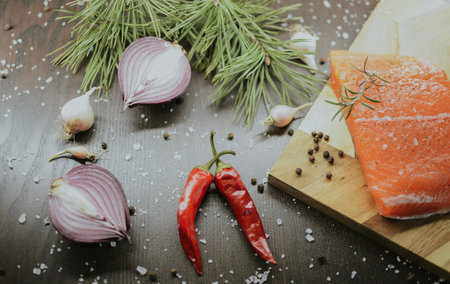 Fresh red salmon on a wooden tray with coarse pepper, salt, garlic, red onion, red pepper and...