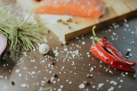 Fresh red salmon on a wooden tray with coarse pepper, salt, garlic, red onion, red pepper and rosemary for the chef to prepare the dish. Close-up on a brown background. High quality photoの写真素材