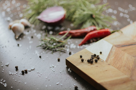 Coarse pepper on a wooden tray with salt, garlic, red onion, red pepper and rosemary for the chef to prepare the dish. Close-up on a brown background. High quality photoの写真素材