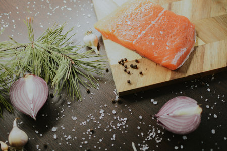 Fresh red salmon on a wooden tray with coarse pepper, salt, garlic, red onion, red pepper and rosemary for the chef to prepare the dish. Close-up on a brown background. High quality photoの写真素材