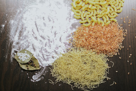 Types of pasta and pink rice with flour, bay leaf with coarse salt and pepper on a brown background close up. High quality photoの写真素材