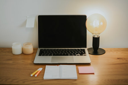 Working wooden table with laptop with black blank screen and calendar, table lamp, candles and felt-tip pens. Workspace for studying at home. High quality photoの写真素材