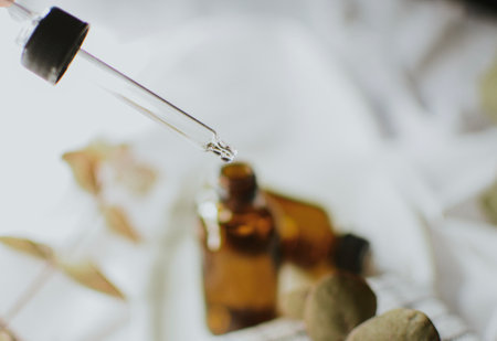 Brown open cosmetic jar with pipette for serum close-up on a white saucer with a checkered towel and eucalyptus on a white fabric background.の写真素材