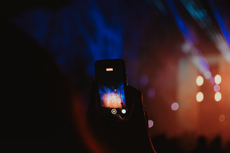 Phone of a concert viewer who is filming the stage with colorful spotlights for atmosphere at night. Close-up. High quality photoの写真素材