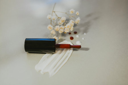Red nail polish brush close-up against a smear of cream on a gray background with white flowers.の写真素材