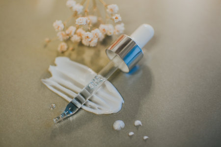 Pipette from a cosmetic jar with serum close-up against a smear of cream on a gray background with white flowers. High quality photoの写真素材