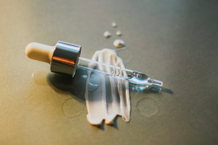Pipette from a cosmetic jar with serum close-up against a smear of cream on a gray background. High quality photoの写真素材