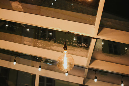 A glowing light bulb hangs from a string under a wooden structure with a glass roof, creating a cozy...