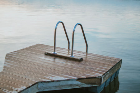 A wooden bridge with an iron staircase leading to the clear water of the lake. It's a summer day, the water is clean and calm, creating an atmosphere of privacy and relaxation in nature.の写真素材