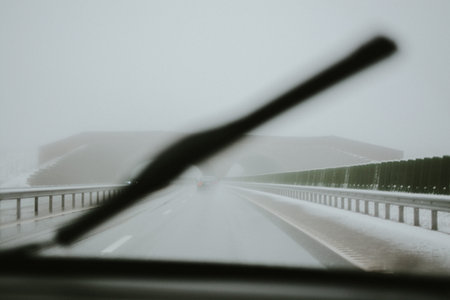 Winter road with a bridge, covered with snow, view from a car through the windshield with a wiper....