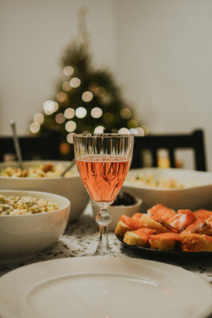 Festive Christmas table with pink wine, appetizers, and salads. In the background, a decorated tree with lights creates a cozy and New Year's atmosphere. High quality photoの写真素材