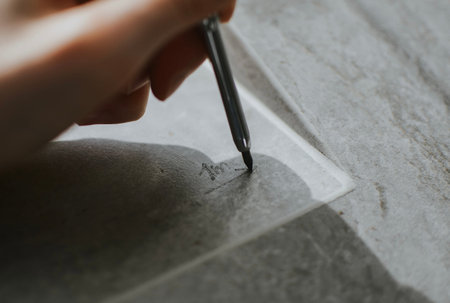 A hand holding a graphite pencil, drawing or marking on a ceramic tile. The image showcases tools...