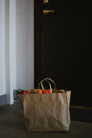 A paper bag with fresh vegetables in the entrance close-up. Order goods from the online store directly to your home via courier using contactless delivery. High quality photoの写真素材