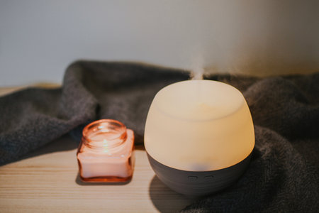 Aroma oil diffuser and pink candle against a backdrop of textured gray fabric in a cozy home. Aromatherapy promotes good sleep and fresh air in the room. High quality photoの写真素材