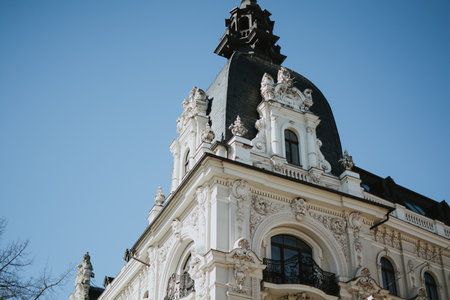 An elegant historic building with a white neo-Renaissance facade and an antique dark roof. Rich architectural decoration, arched windows, graceful columns and a balcony, metal fencingの写真素材