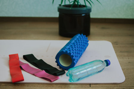 Light exercise mat with exercise equipment in the form of rubber bands, foam roller and bottle of...