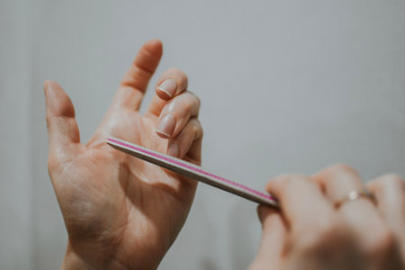 Woman removes nail length with nail file by herself at home. File nails, body hygiene. High quality photoの写真素材